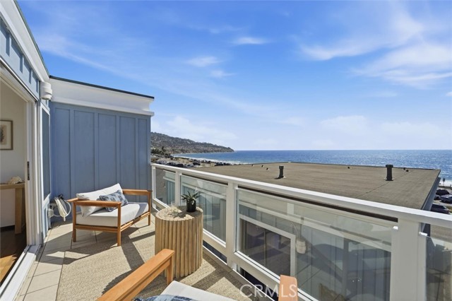 Balcony with two wooden chairs and a small table overlooking the ocean and clear blue sky.