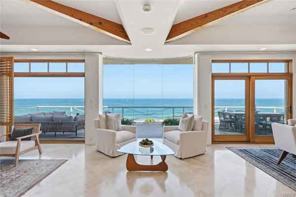 Luxurious living room with white seating and a glass coffee table overlooking an ocean view through large glass doors.