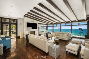 Luxurious coastal living room with white sofas, dark wood floors, and a panoramic ocean view through curved glass—bright and modern.