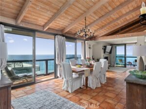 Ocean-view dining room with a wood-beam ceiling, tile floor, and a table set for eight by sliding glass doors to a balcony over the sea.